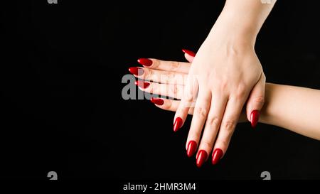 Crop woman touching hands. Crop hand of anonymous female with red manicure on black background in dark studio. Stock Photo