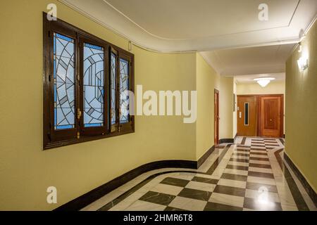 Entrance hall of an old residential apartment building checkered marble floors, elevator and leaded glass window Stock Photo