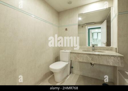 Bathroom decorated with cream colored faux marble tiles and marble veined sink countertop with square frameless mirror in vacation rental home Stock Photo