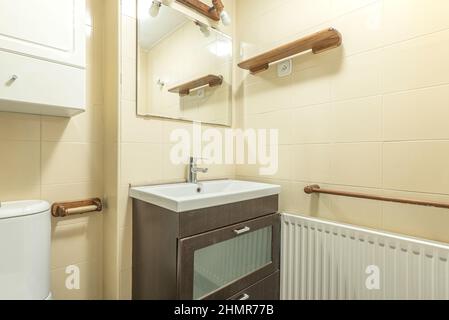 Bathroom with dark wood furniture and white porcelain sink, square mirror and aluminum radiator Stock Photo