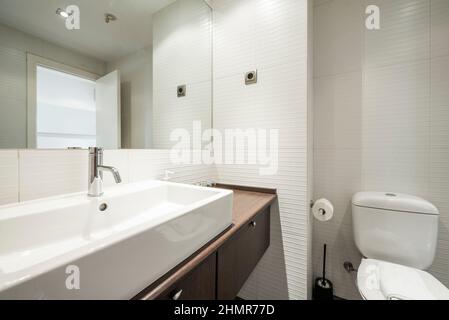 Bathroom with dark wood cabinets with drawers and white porcelain sink, rectangular frameless mirror Stock Photo