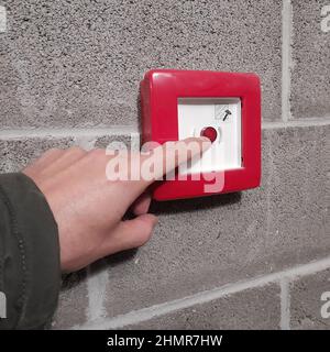 Closeup of a person pressing the red emergency button on the wall outdoors Stock Photo
