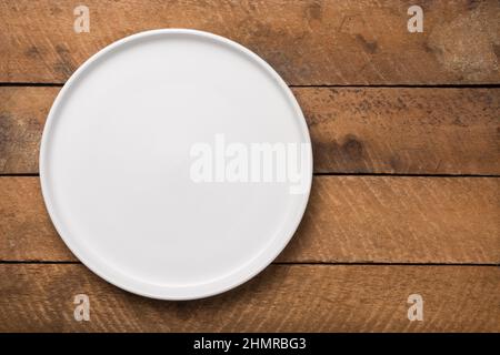 empty white plate on a wooden table top, food photography background or backdrop, horizontal top view with copy space Stock Photo