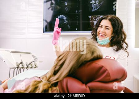 Stomotologist woman happy smiling at her work and showing two fingers up while working with a patient in a clinic. Stock Photo
