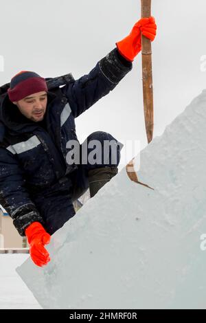 The installer stands on the ice block holding on to the tape sling Stock Photo