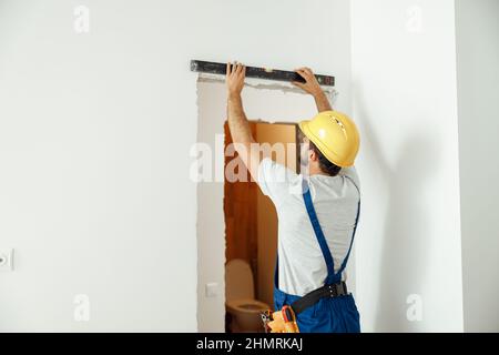 Professional handyman, male worker in uniform using spirit level while taking measurements indoors Stock Photo