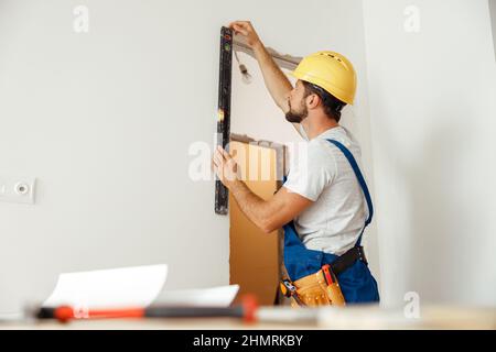 Hard working handyman, builder in uniform measuring the wall using bubble level Stock Photo