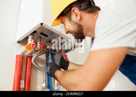 Closeup of plumber using screwdriver while fixing boiler or water heater, working on heating system in apartment Stock Photo