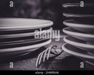 The detail of a fork between two piles of stacked plates, in black and white Stock Photo