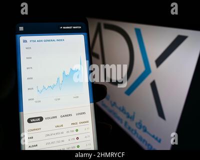 Person holding smartphone with webpage of company Abu Dhabi Securities Exchange (ADX) on screen with logo. Focus on center of phone display. Stock Photo