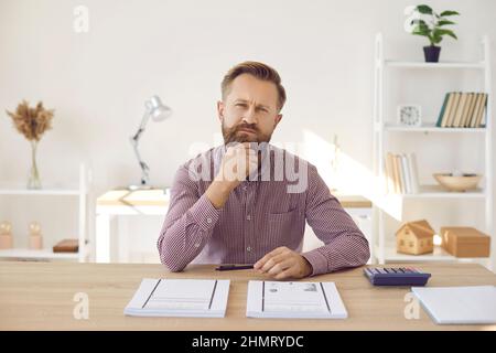 Portrait of focused pensive businessman looking at camera while sitting in office. Stock Photo