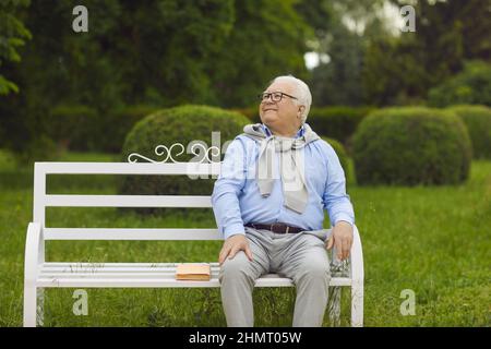 Happy carefree senior man sitting on wooden bench relaxing on sunny day in park Stock Photo