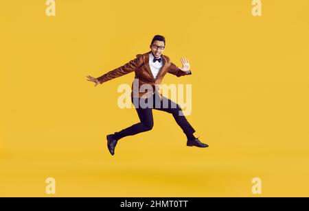 Happy funny young guy in leopard jacket jumping in air isolated on yellow background Stock Photo