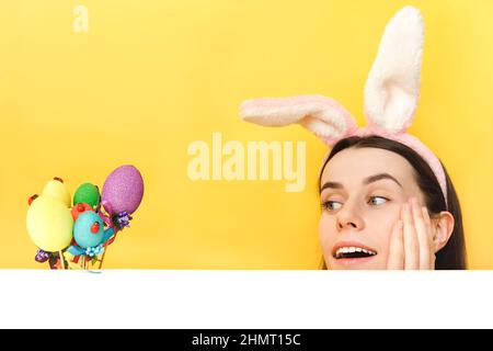 Close up portrait of pretty impressed young caucasian woman wear bunny fluffy ears, shocked fun looking at easter colorful eggs, posing isolated over Stock Photo