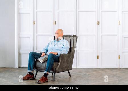 Stylish thoughtful mature businessman sitting in leather armchair with notebook Stock Photo