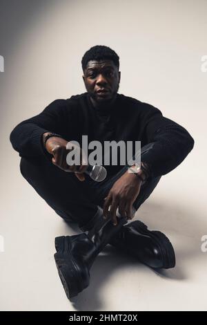 black man with microphone looking at the camera sitting white background - full shot. High-quality photo Stock Photo