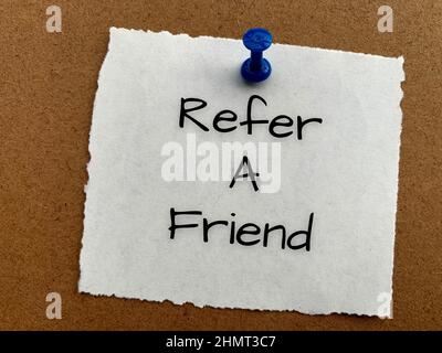 Refer a friend text on white notepad. Stock Photo