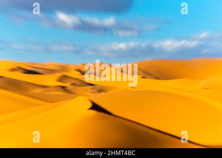 Motion blur effect of a landscape in the Sahara Desert. Golden yellow sand dunes in foreground, blurred moving clouds and blue sky background. Stock Photo