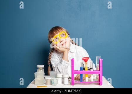 Cute student child girl with science experiment thinking, dreaming and looking up on blue Stock Photo