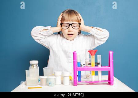 Funny kid schoolgirl doing science experiments on blue background. Science and education concept Stock Photo