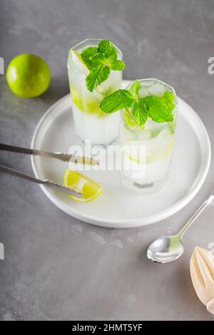 Cocktail mojito and bar accessories on gray background. Two highball glasses of mojito on a white plate. Summer cocktail with lime and mint Stock Photo