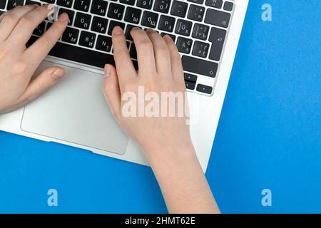 Female hands and laptop keyboard on blue background. Concept workspace, work at the computer, freelance and design. Flat lay, top view and copy space Stock Photo