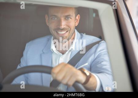 A male customer is sitting in the new car he just bought at auto shop and posing for a photo in a happy manner. Car, shop, buying Stock Photo
