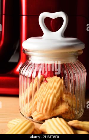 Heart shaped cover. Homemade biscuits and a jar on a pastry board. A red mixer in the background. Stock Photo