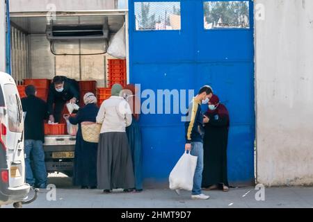 People holding grocery bags to buy milk packs in the street sidewalk, a truck parked with doors opened a man is selling plenty of milk crates inside. Stock Photo