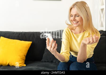 Happy beautiful senior woman is using a smartphone for video calling to family, friends or dating online. Mature elderly lady holds the phone and using app for video communication, online meeting Stock Photo