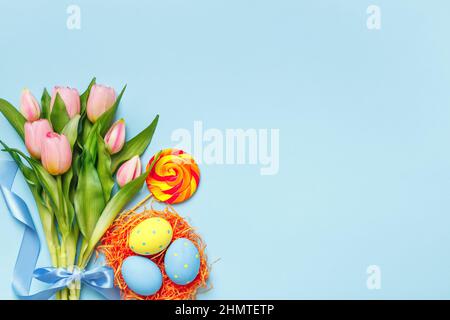 Easter eggs in a nest candy bouquet of pink tulips on a blue background. Flat lay copy space top view. Stock Photo