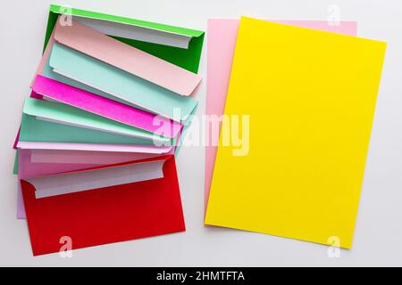 Multicolored envelopes with blank yellow sheet of paper, greeting card or invitation mockup Stock Photo