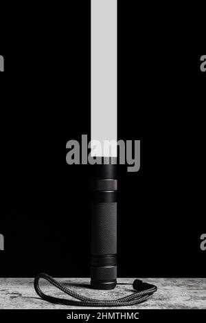 Flashlight stands on a table with a narrow beam of light upwards on a black background. Stock Photo