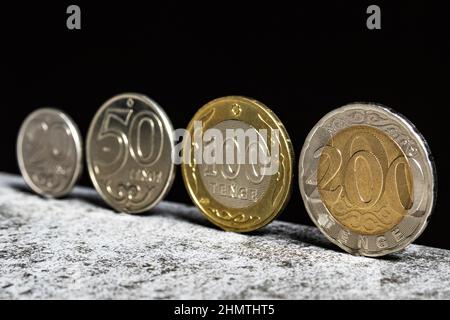 Kazakh coins in denominations of 20, 50, 100 and 200 tenge stand on a table on a black background. Stock Photo