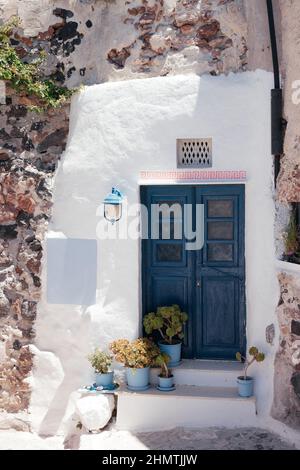 Beautiful blue door on white and stone facade with flowers in pots of greek architecture in Oia city, Santorini island, Greece, Europe. Beautiful deta Stock Photo