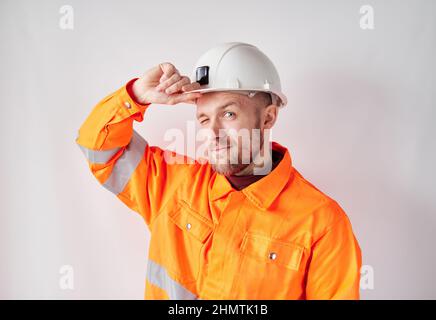 Cheerful looking at camera young caucasian engineer, worker, supervisor or building contractor in white helmet and orange jacket correcting his hardhat. Building industry concept. High quality image Stock Photo