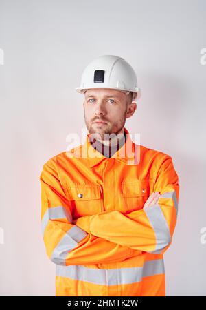 Attractive serious bearded male supervisor, engineer or construction worker in white hard hat and safety orange reflective vest. Young foreman or technician in hard hat. High quality vertical photo Stock Photo