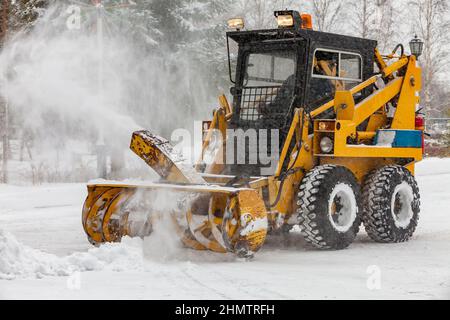 Tractor with snow plow blade clears road in city from fresh fallen snow. Snowplow removing snow on street after blizzard. Snowplow vehicle clears snow Stock Photo