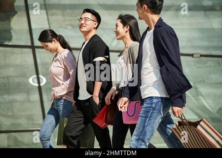 high angle view of group of four young asian people chatting talking conversing while walking on street with shopping bags in hands Stock Photo