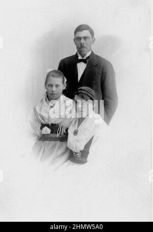 20th century authentic vintage photograph of young man in suit and bow tie and two young women in traditional costume, Sweden Stock Photo