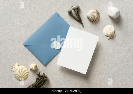 Elegant wedding invitation card and blue envelope with seashells on beige background. Nautical wedding, sea, marine concept. Stock Photo