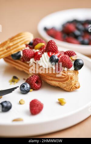 Eclair cake. Sweet delicious eclairs, traditional French pastries with cream and decorated with raspberries, blackberries. Copy space for text. Mornin Stock Photo