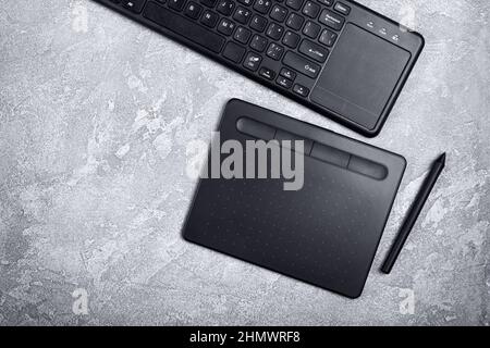 Top view of designer work place with graphics tablet and keyboard on grey concrete background Stock Photo