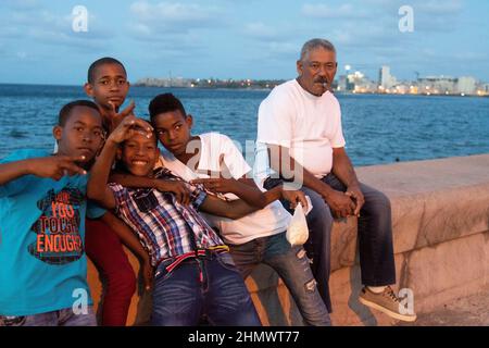 Man smoking cigar sitting with young boy, one holding a bag of popcorn on the malecon seafront in Havana, Cuba. Stock Photo