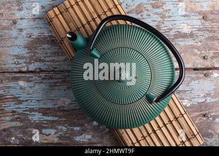 Traditional green asian cast iron kettle on bamboo mat and old blue wooden background Stock Photo