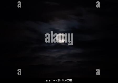 Moon rising against black sky with clouds at night Stock Photo