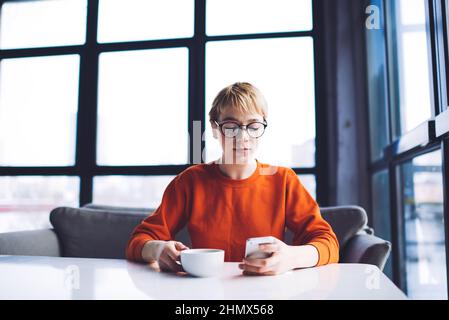Thoughtful woman with cup of coffee using smartphone Stock Photo