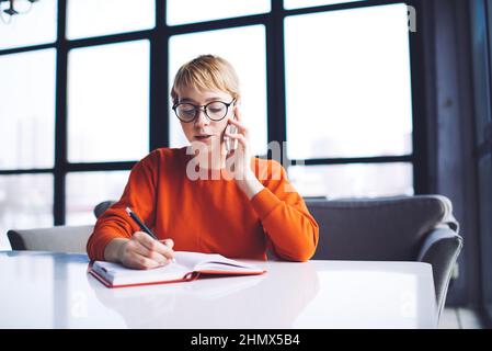 Thoughtful woman writing notes while making phone call Stock Photo