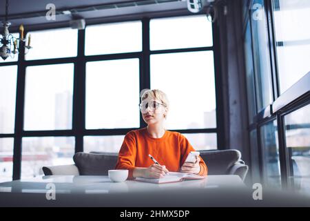 Thoughtful woman with notebook and smartphone spending time in cafe Stock Photo