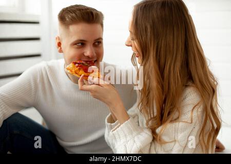 Romantic relationship of young couple in love. Beautiful long haired brown-haired woman feeds her friend pizza, it gives them great pleasure. Concept Stock Photo